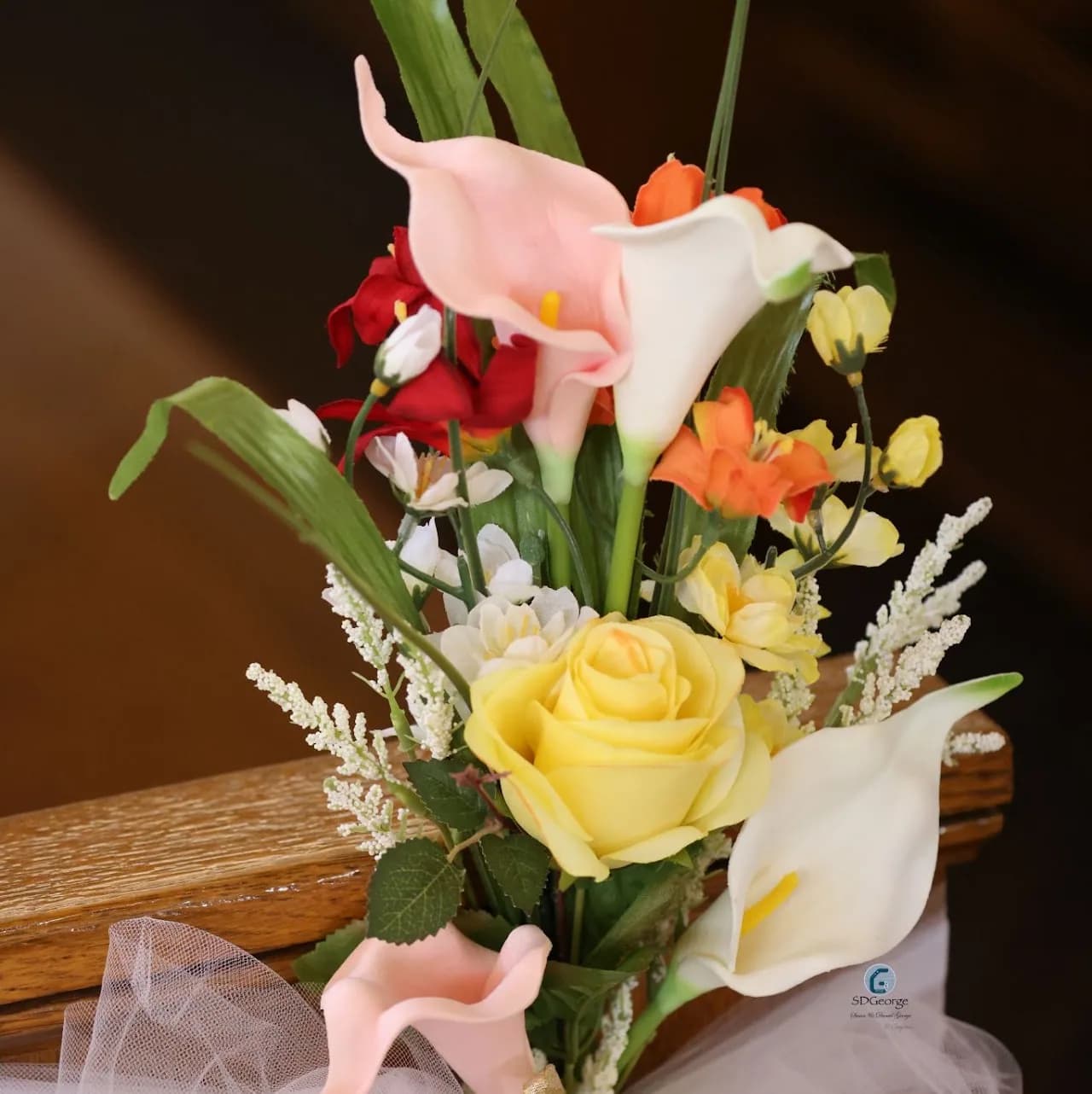 Close-up of calla lilies and a yellow rose in a tulle-tied pew-end flower arrangement