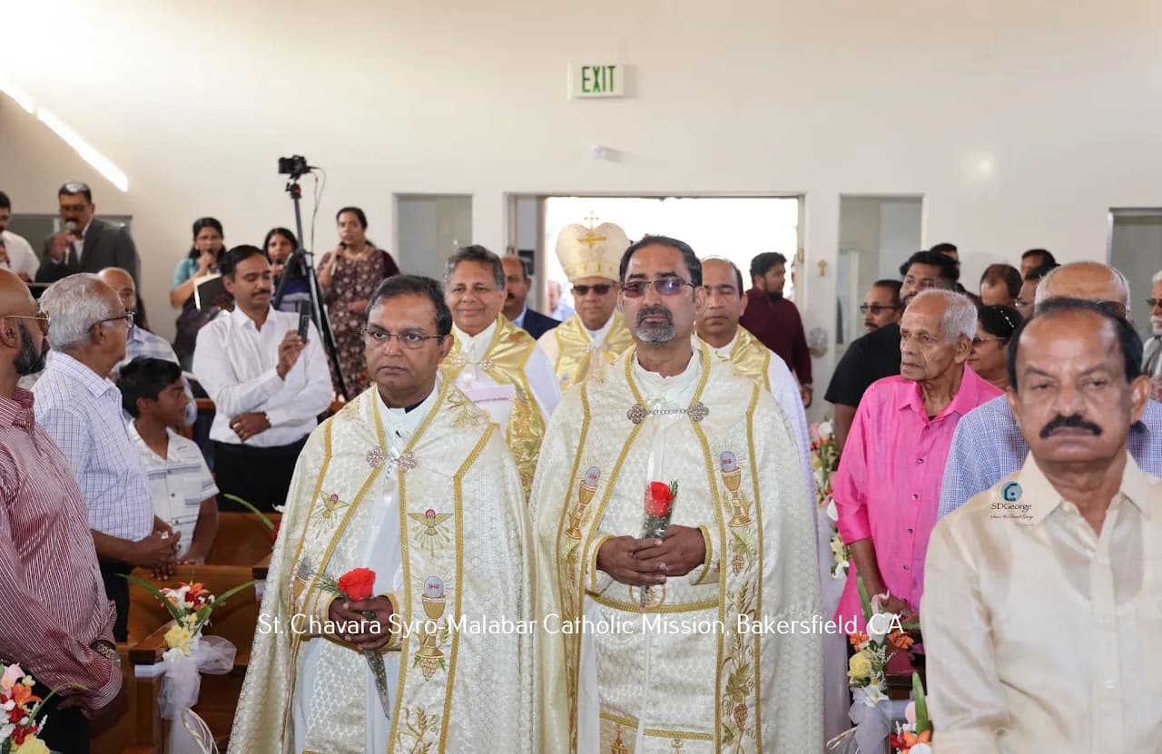 Two priests in gold vestments processing down the aisle holding red roses, bishop behind them