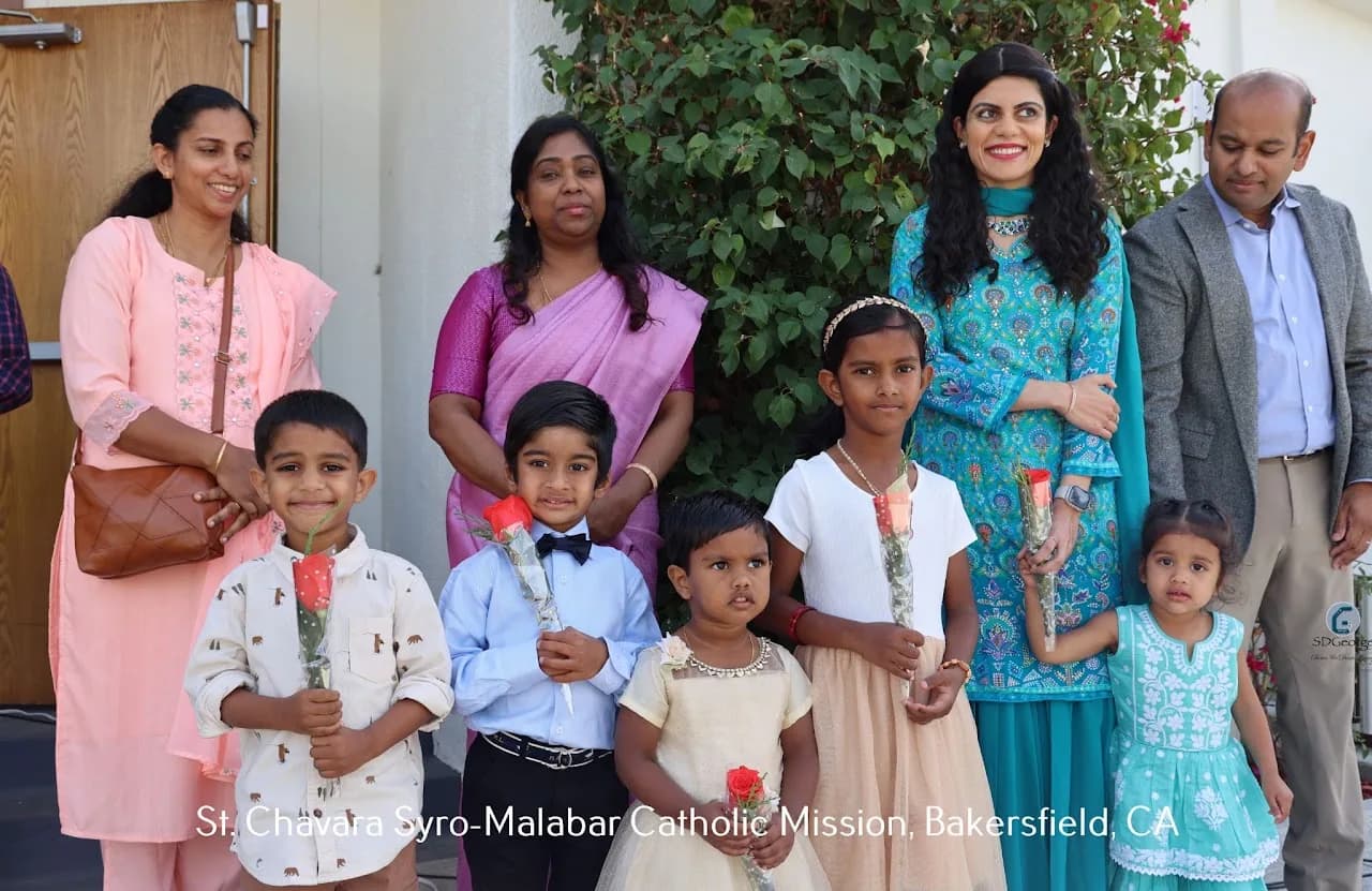 Four adults standing behind five children holding red roses outside the church entrance