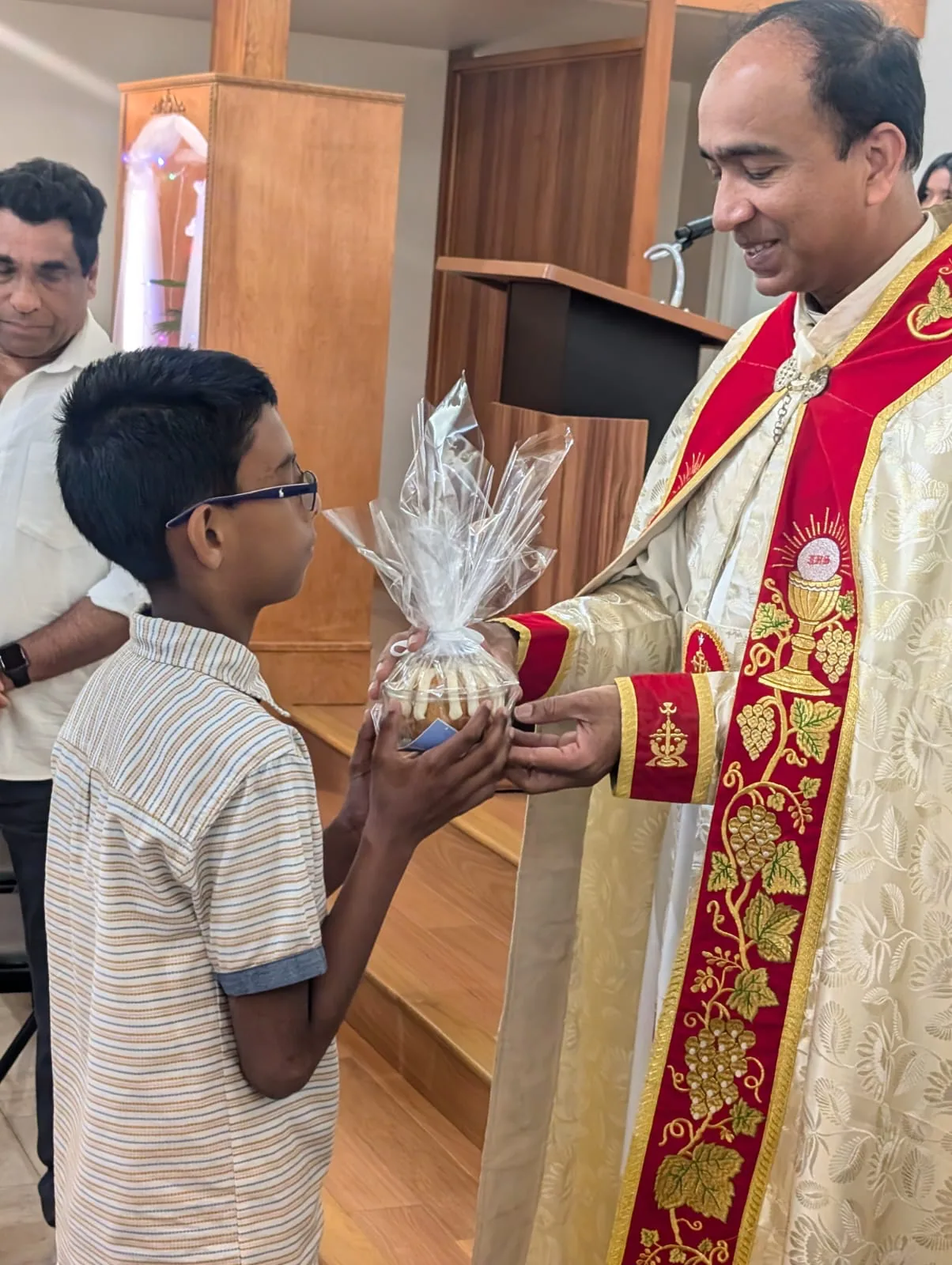 Boy receiving a wrapped gift basket from a priest in red and gold vestments
