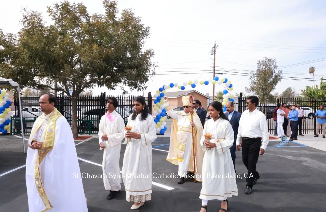 Priest, altar servers and a bishop process across the parish parking lot under a balloon arch
