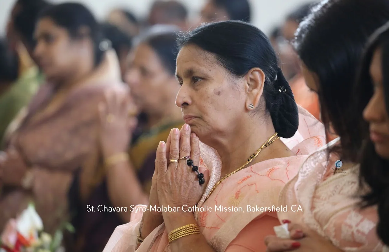 Elderly woman in a peach sari praying with joined hands during Mass