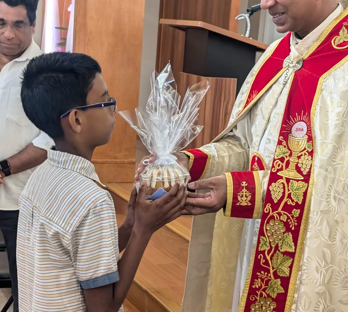 Boy receiving a cellophane-wrapped gift from a priest in red and gold embroidered vestments