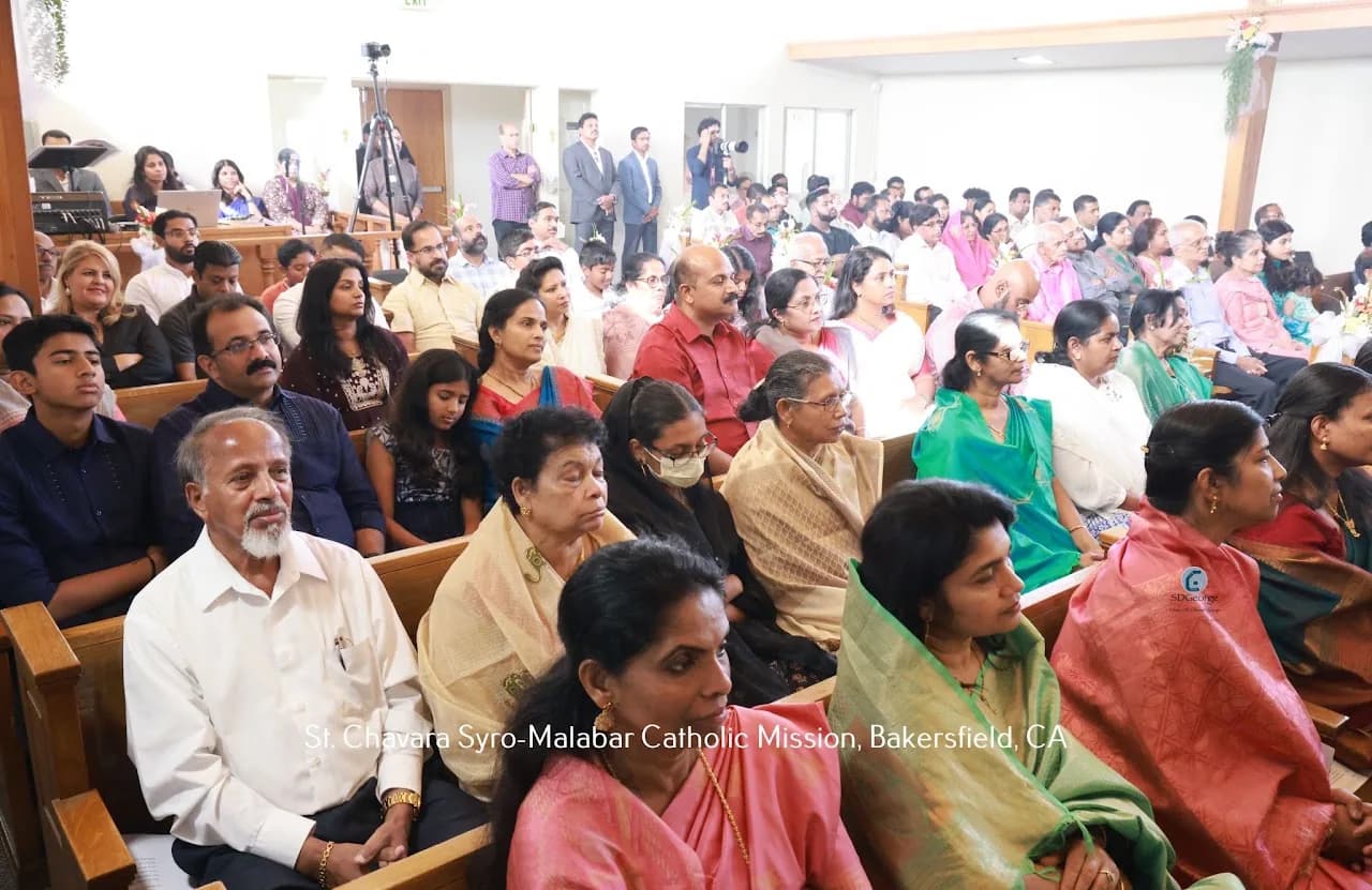 Packed congregation of families in saris and suits seated in wooden pews during Mass