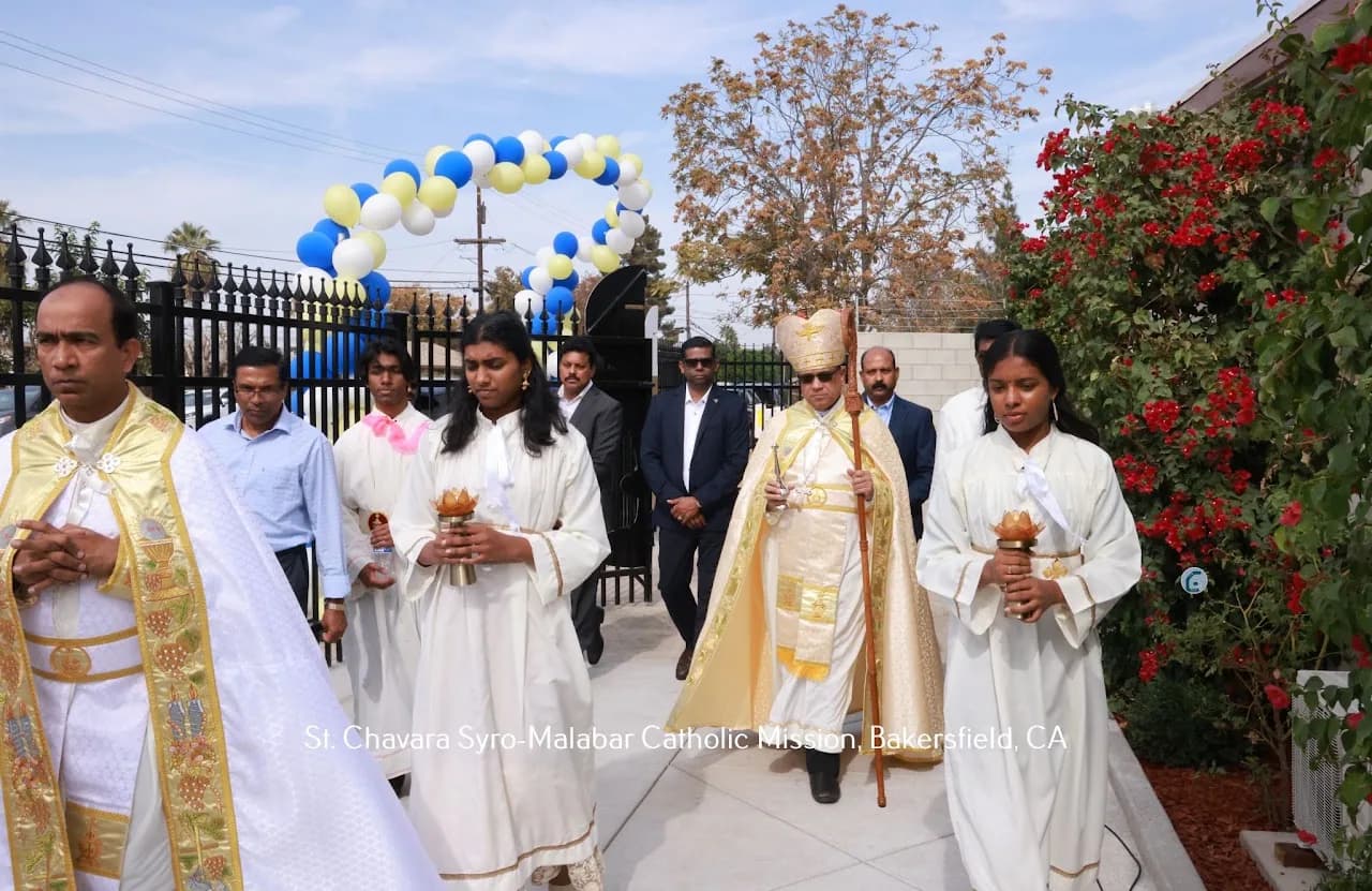 Bishop in gold vestments processing outdoors under a balloon arch with robed altar servers carrying censers