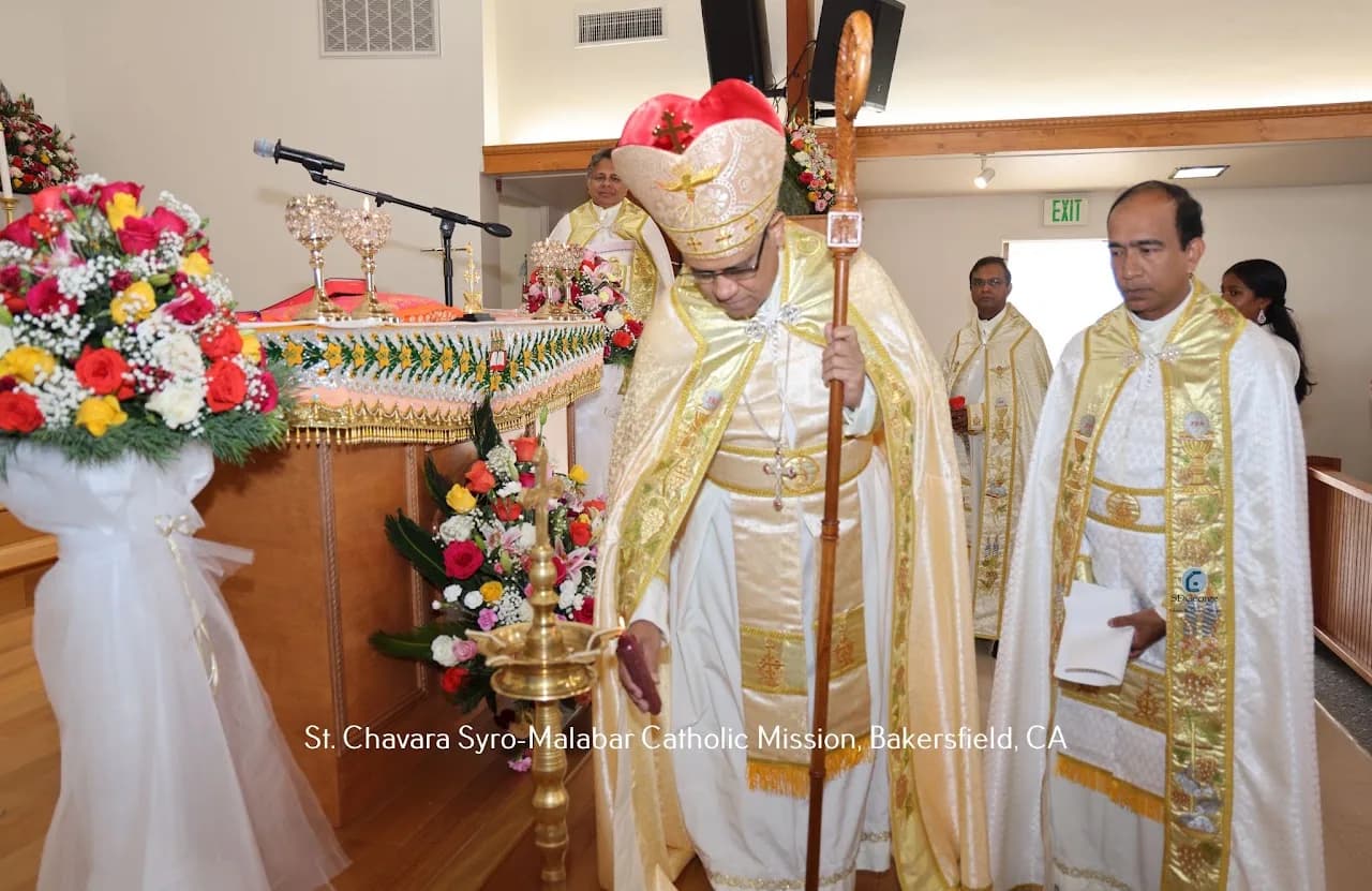 Bishop with crozier bending to light a tall brass oil lamp beside a garlanded altar