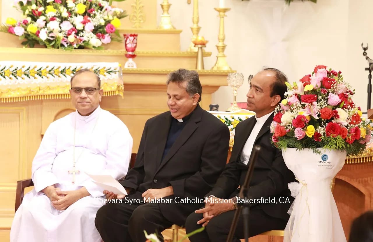 Bishop and two priests seated before a gilded altar with flower arrangements during a ceremony