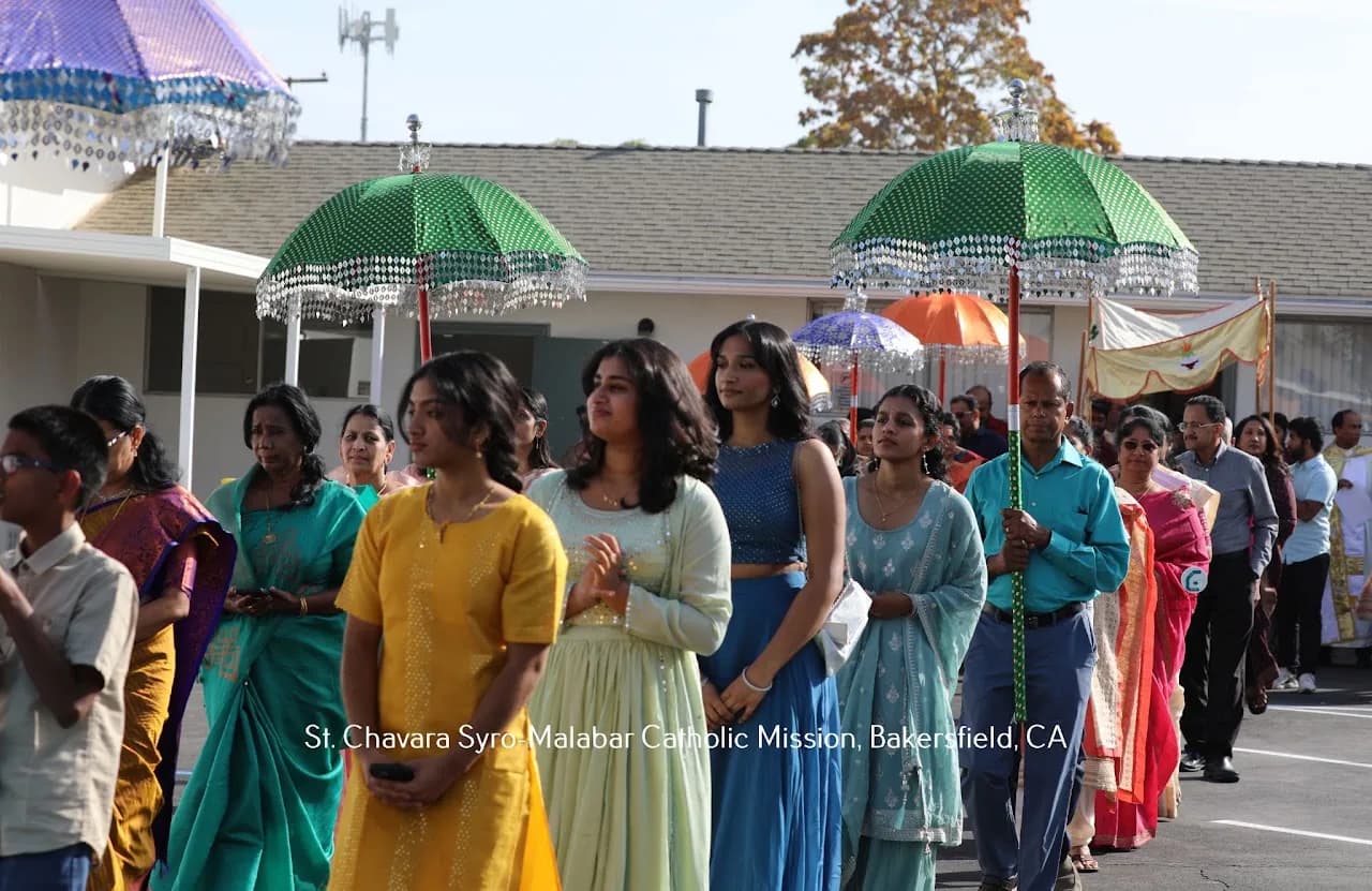 Parishioners in colourful Indian dress processing beneath sequinned ceremonial umbrellas outdoors