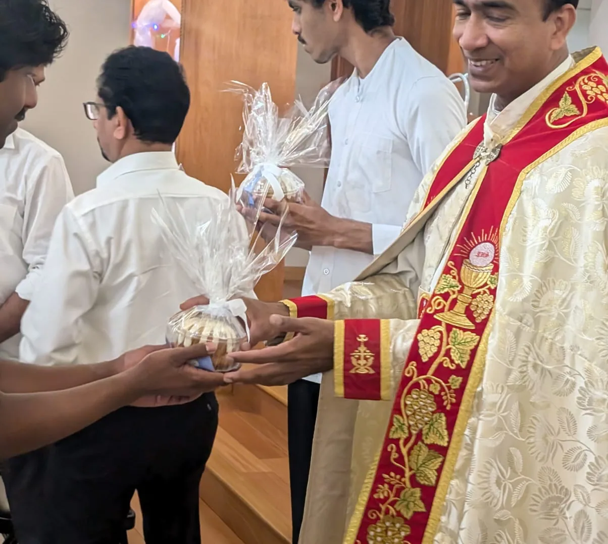 Smiling priest in red vestments distributing wrapped gift baskets to three men
