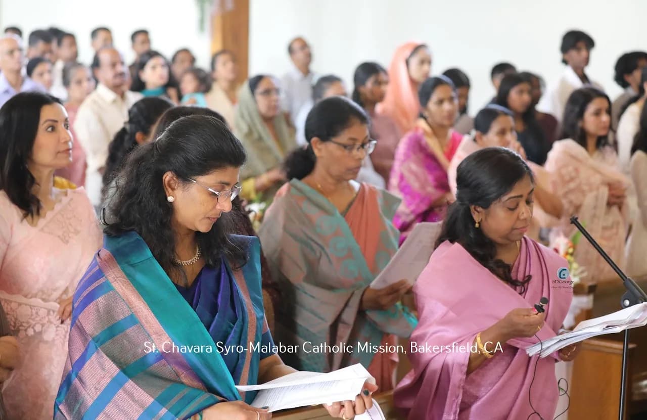 Congregation of women in saris standing in pews reading from printed prayer sheets