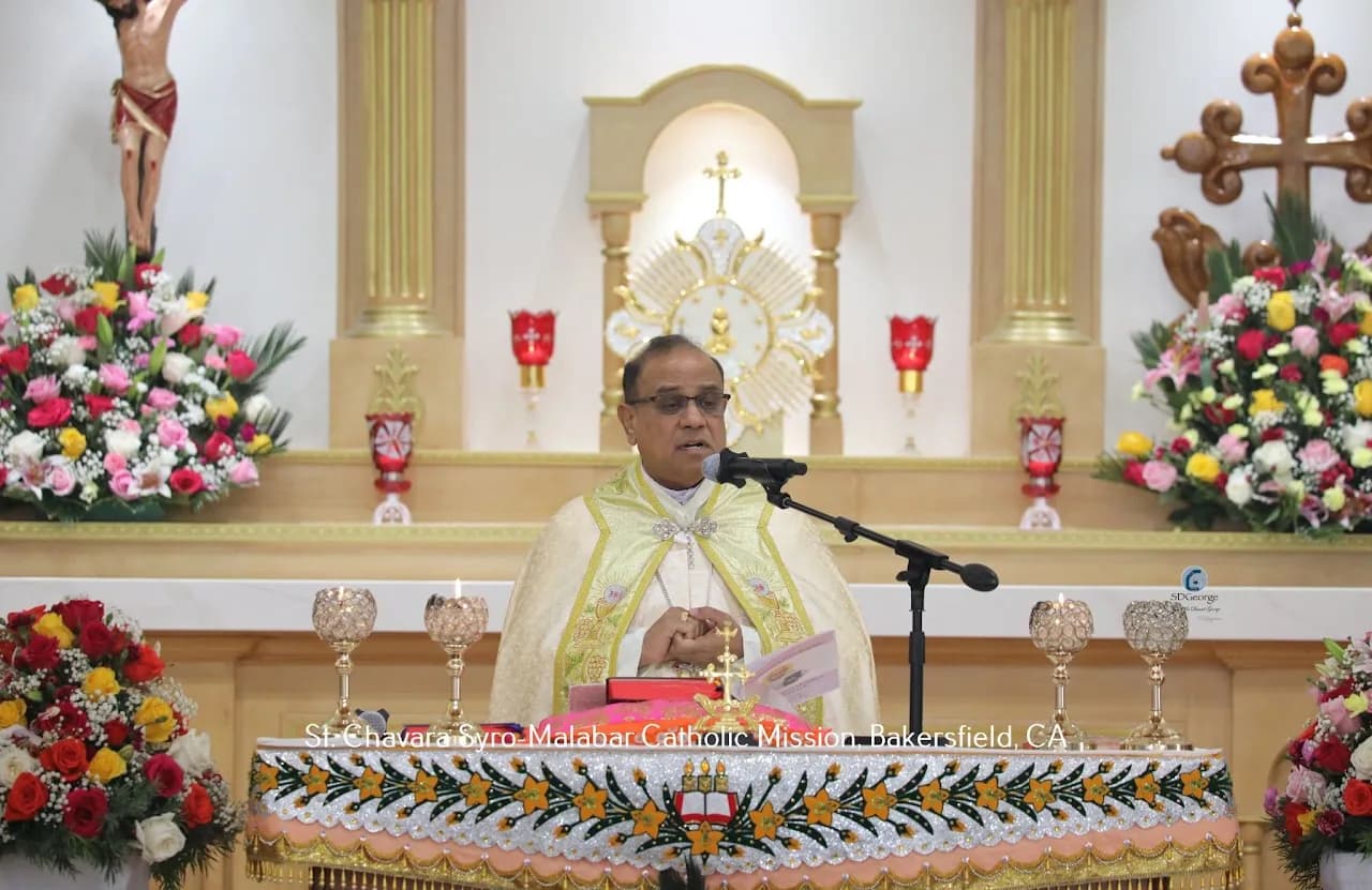 Bishop in gold cope speaking at a microphone before a flower-decorated altar and tabernacle