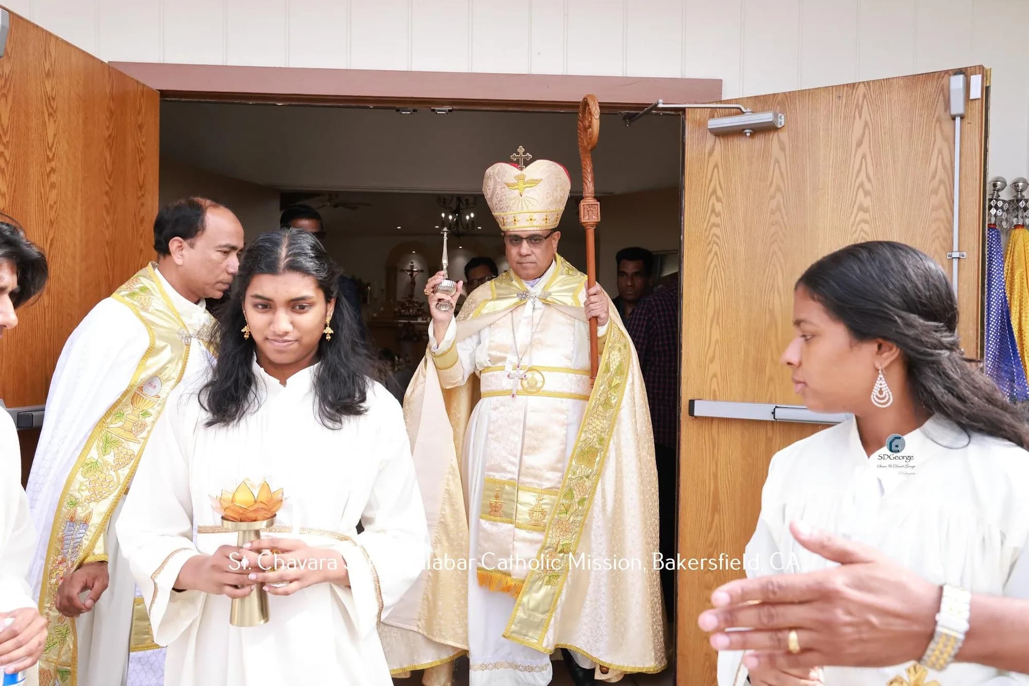 Bishop with crozier and holy water sprinkler processing out the church doors with servers