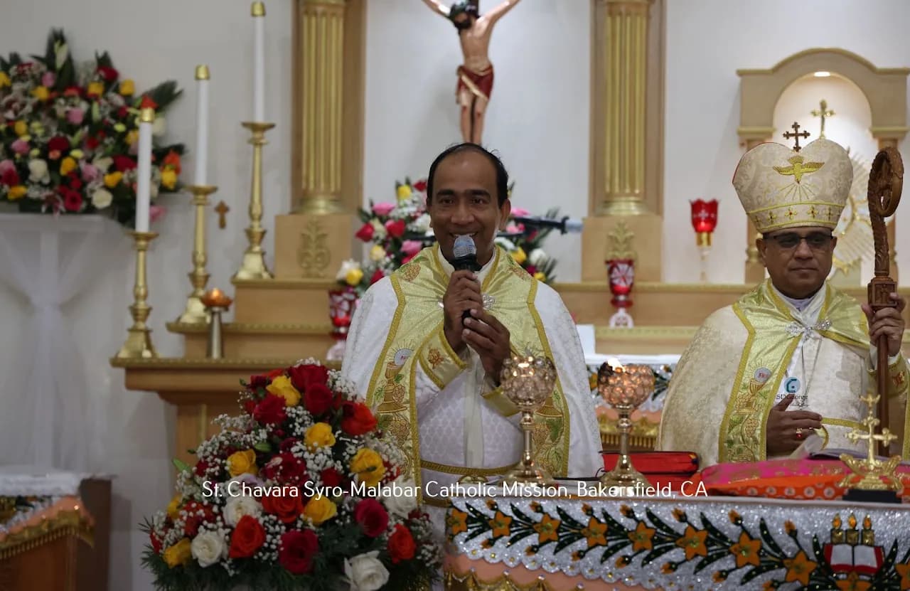 Priest speaking into a microphone at the altar beside a bishop in mitre holding a crozier