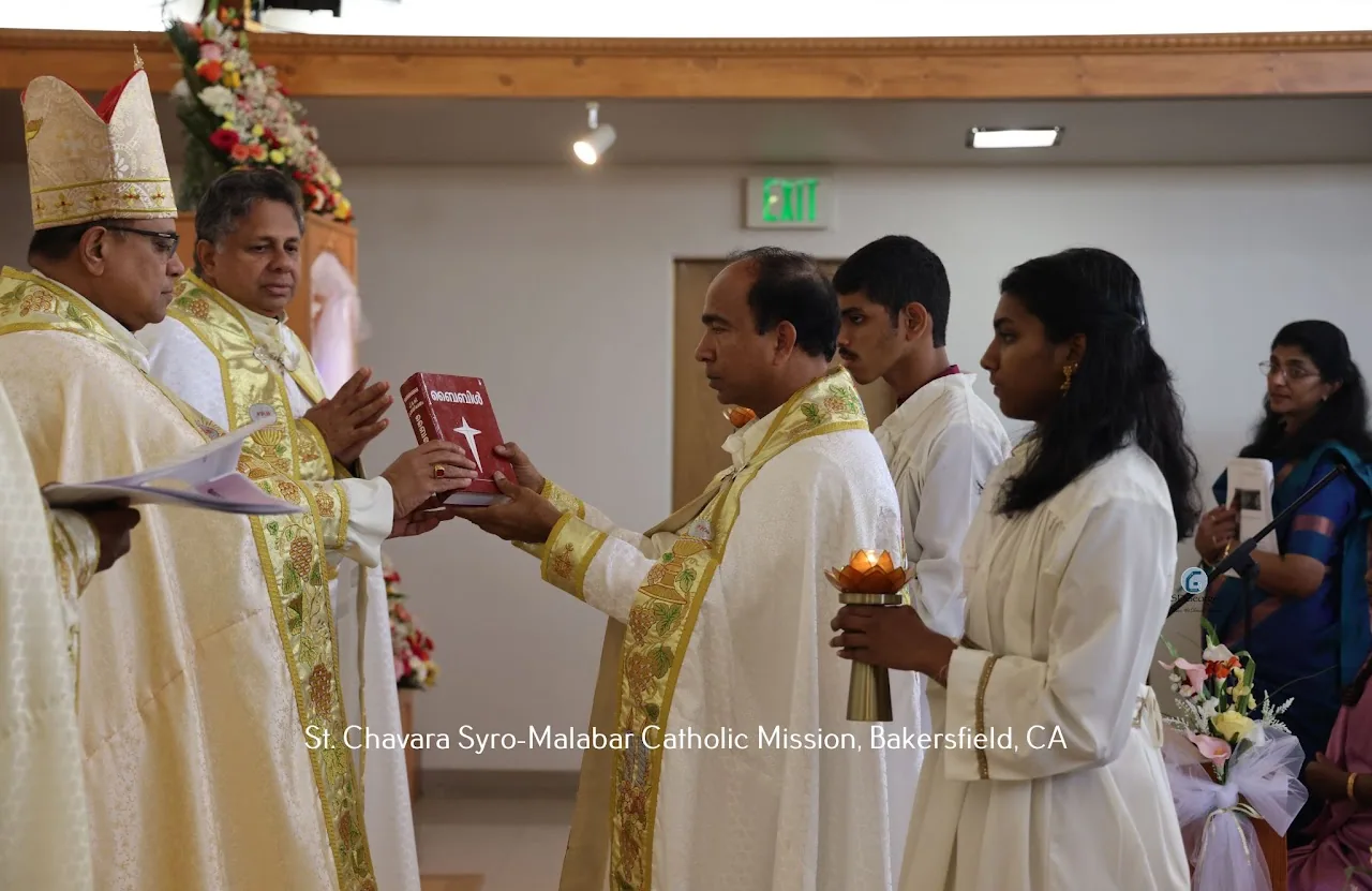 Bishop and priests blessing a red Malayalam Bible held by a vested priest at the altar