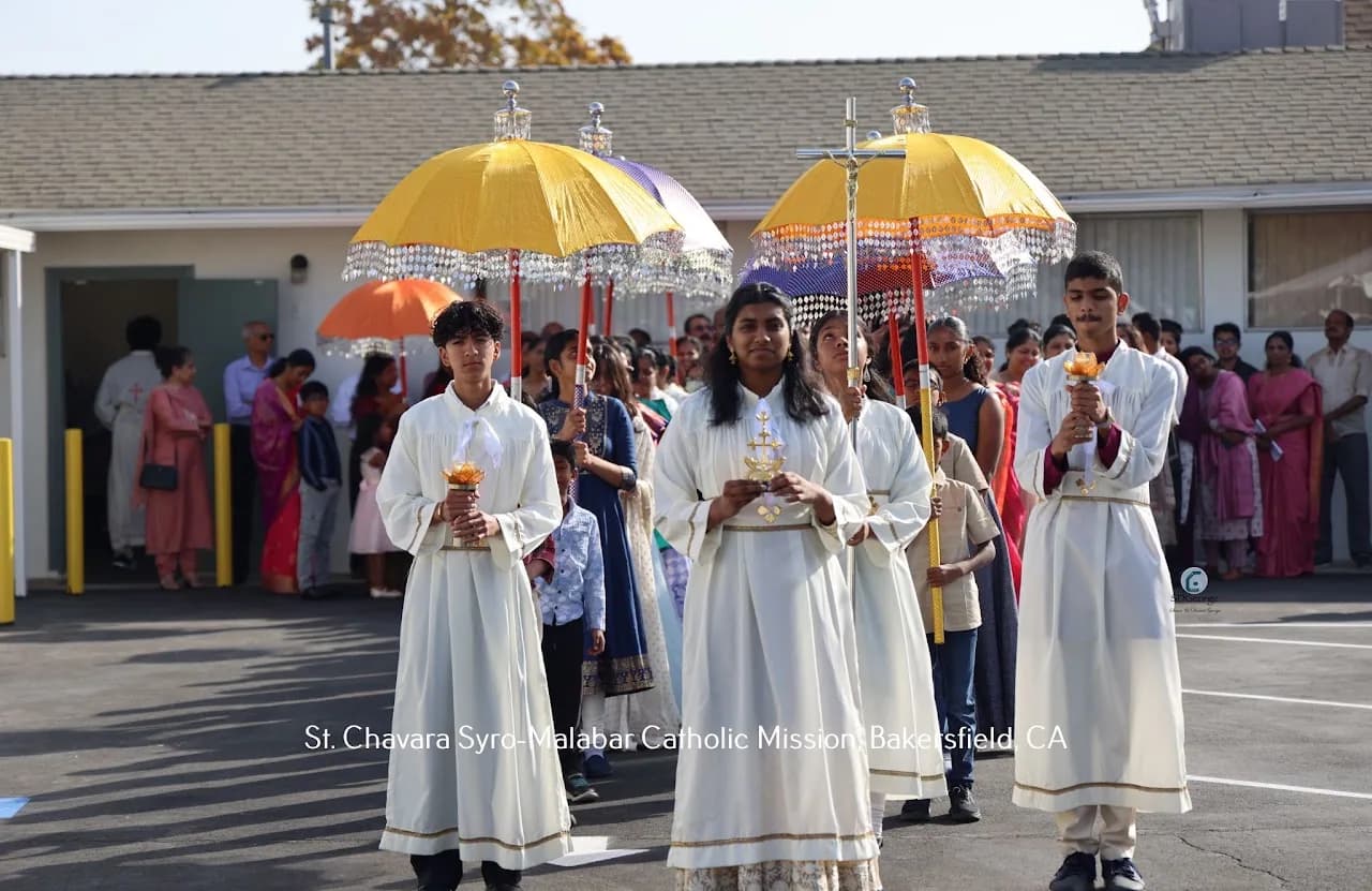 Altar servers with processional cross and lamps lead a parade under fringed Kerala ceremonial umbrellas