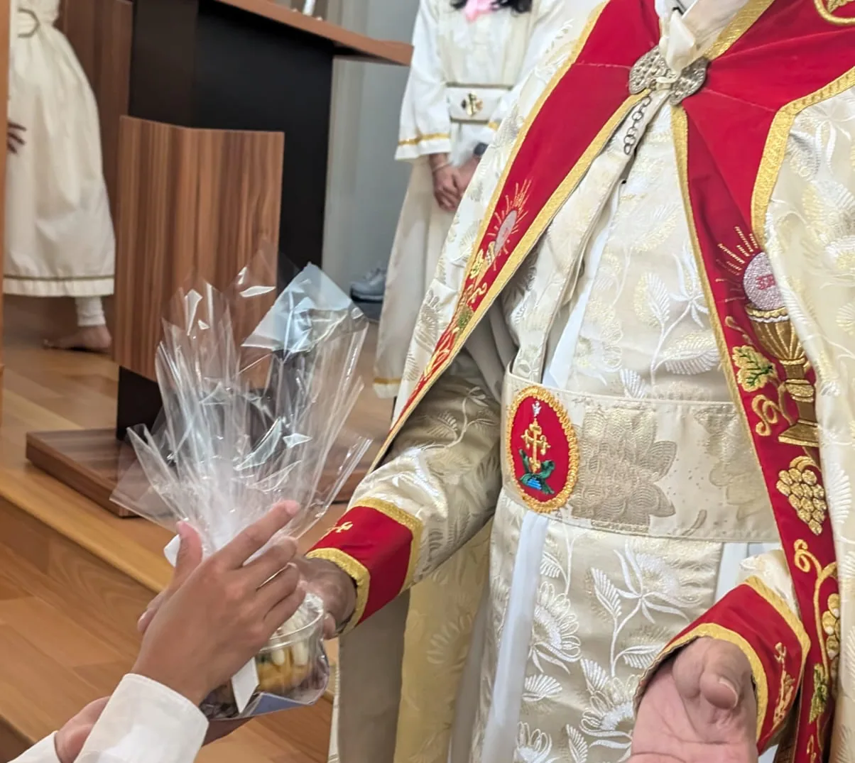 Clergyman in embroidered red and cream vestments receiving a cellophane-wrapped gift