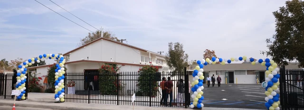 Church exterior behind an iron fence with blue, white and yellow balloon arches at the entrance