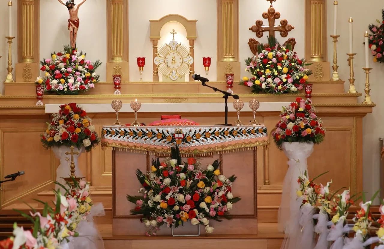 Church altar decorated with six large rose arrangements, gilded sunburst tabernacle, crucifix and Mar Thoma cross