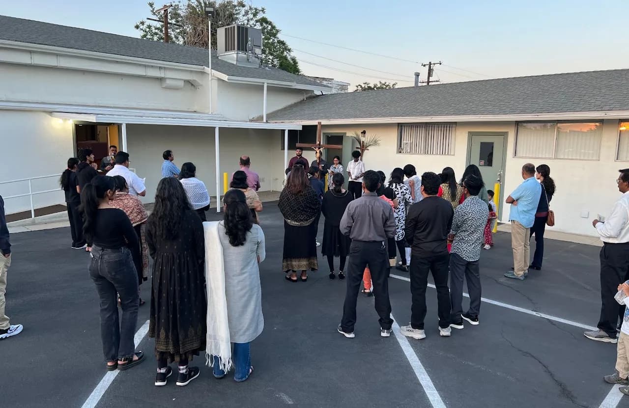 Parishioners gathered in a parking lot at dusk around a young man holding a large wooden crucifix