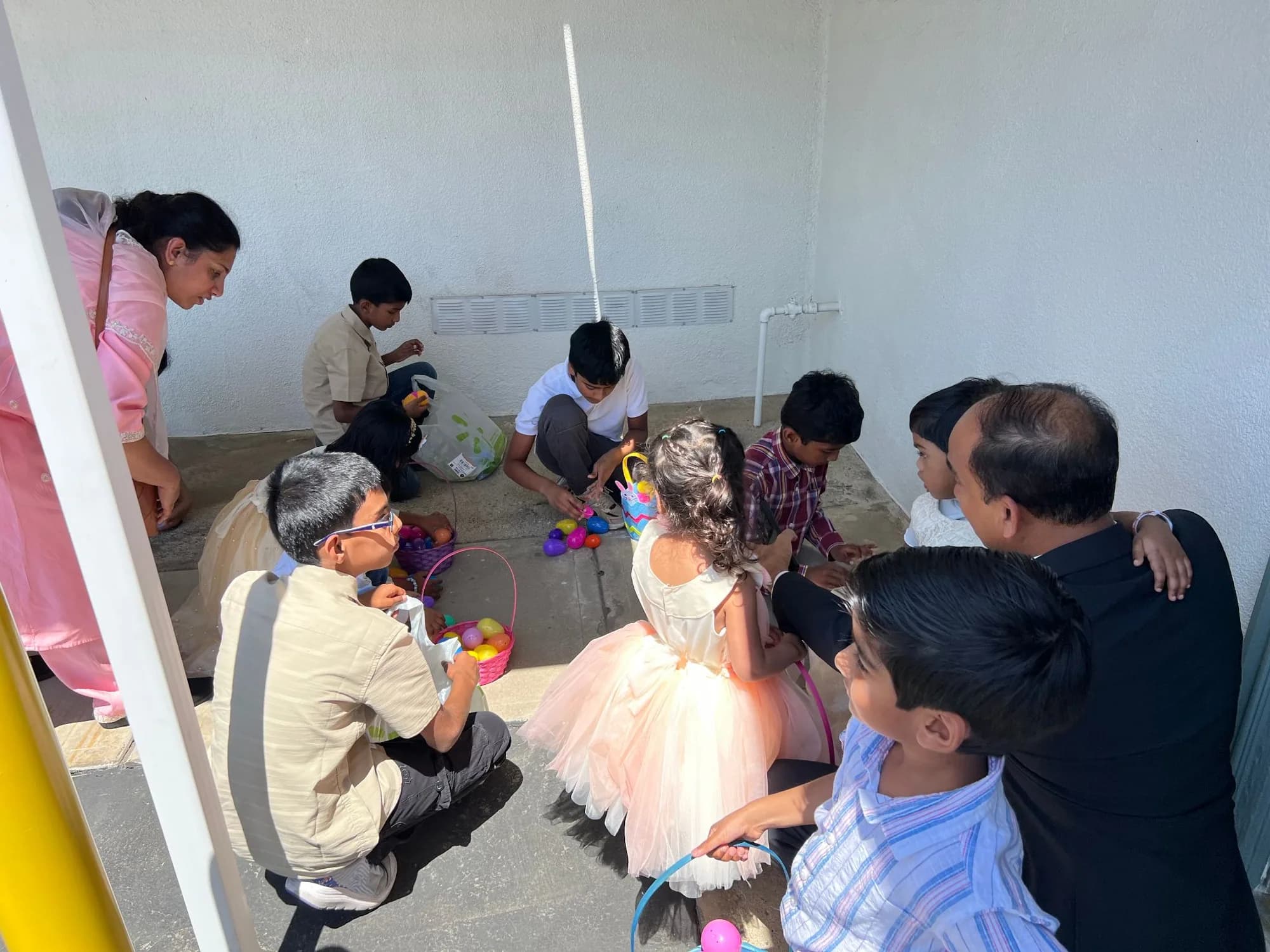 Children crouched on a patio sorting plastic Easter eggs into baskets while adults watch