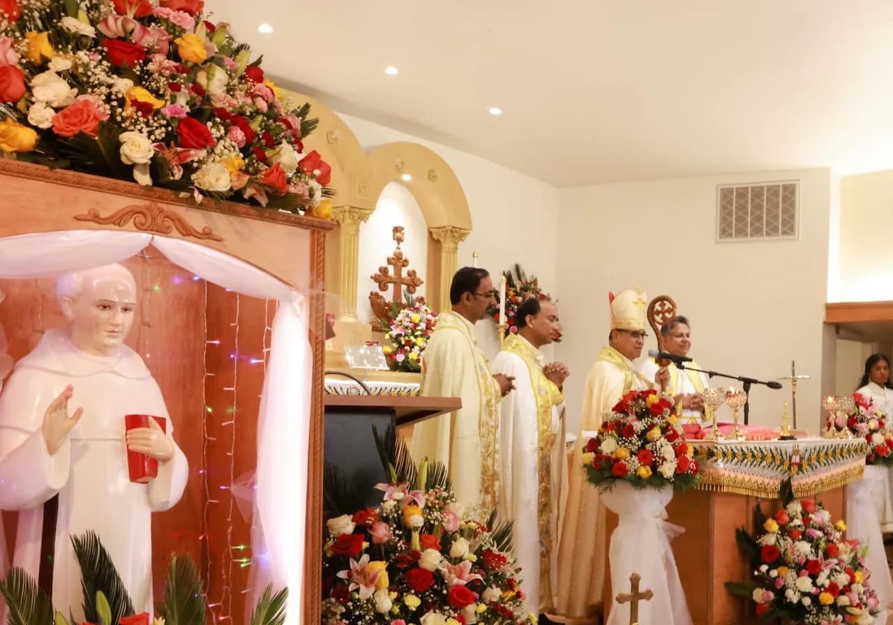 Bishop with crozier and three priests at the altar beside an illuminated statue of St. Chavara